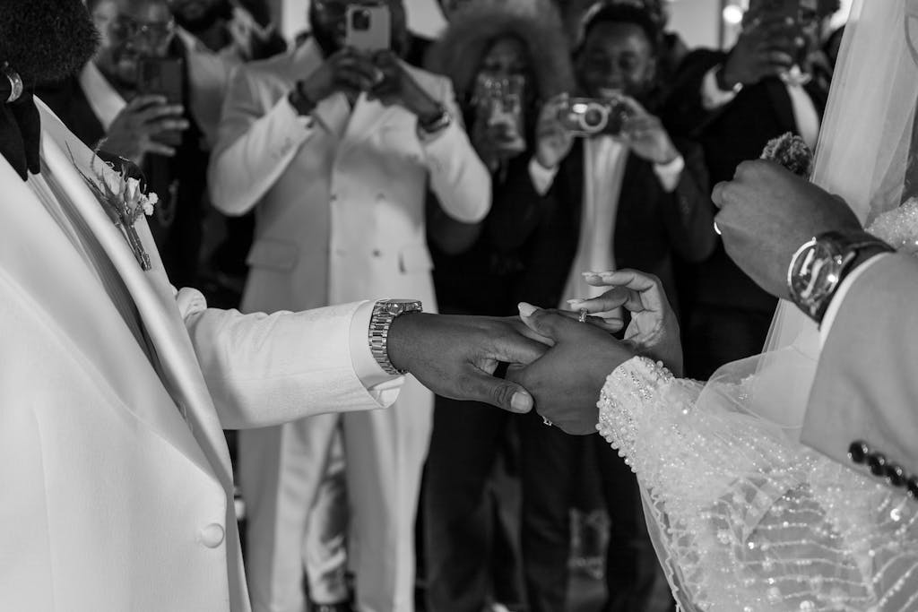 A classic black and white photo capturing a couple exchanging rings during a wedding ceremony.